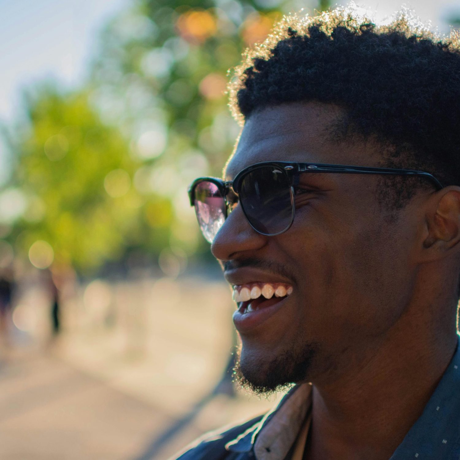 A smiling African American man wearing sunglasses, outdoors on a sunny day.