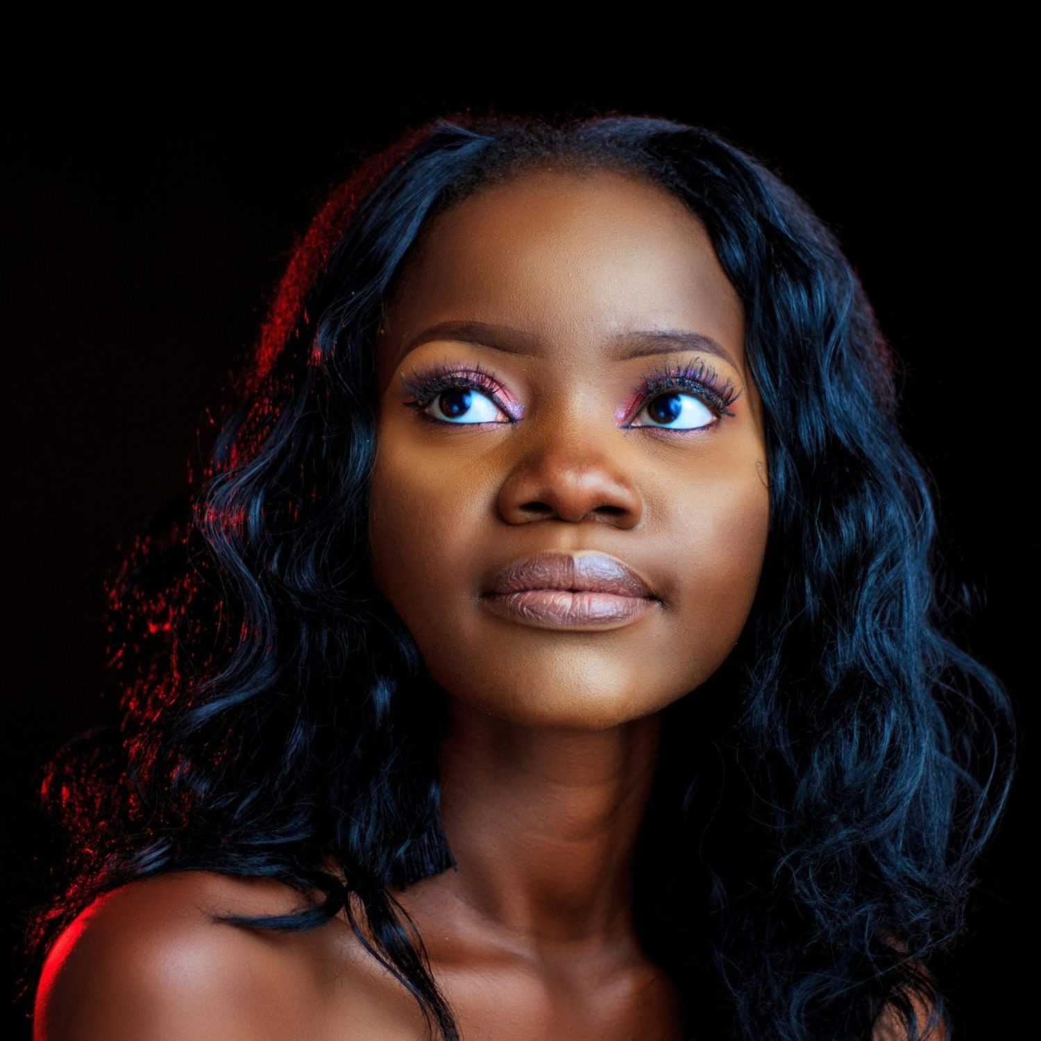 A beautiful portrait of a young black woman with stylish makeup and hairstyle, looking thoughtfully upwards in a studio setting.